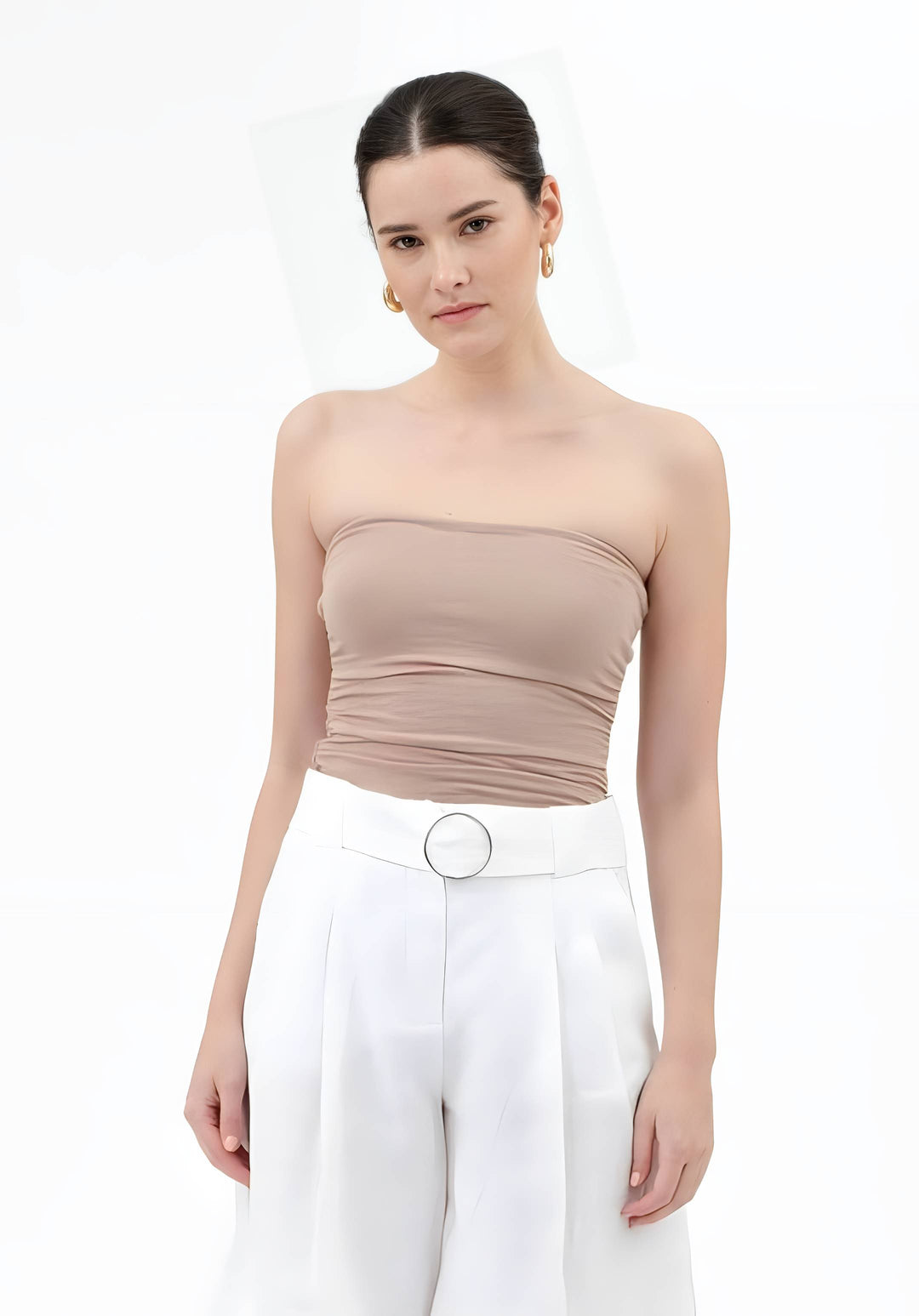 A woman modeling a beige strapless ruched tube top paired with white high-waisted trousers featuring a silver belt, set against a plain white background.