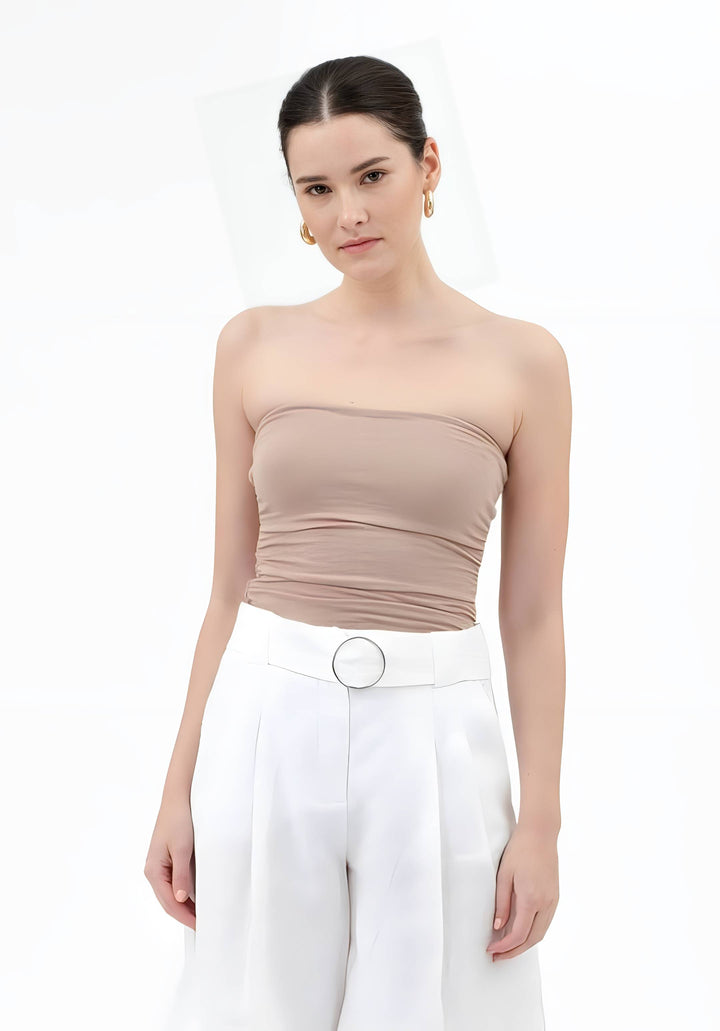 A woman modeling a beige strapless ruched tube top paired with white high-waisted trousers featuring a silver belt, set against a plain white background.