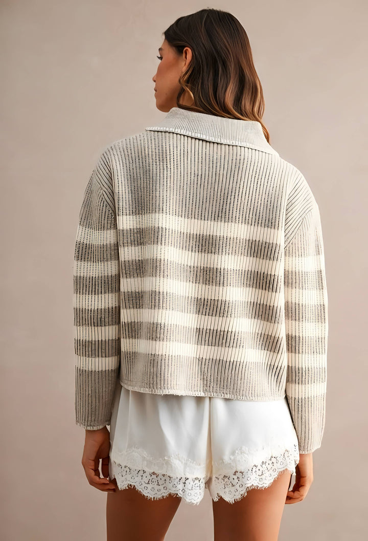 A woman shown from the back wearing a cream and taupe striped ribbed knit cardigan with a high collar, paired with white shorts featuring a lace hem, against a solid beige background.