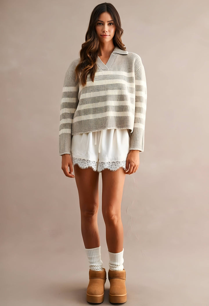 A woman modeling a cozy knit sweater with horizontal beige and white stripes, paired with white lace-trimmed shorts, white socks, and tan platform boots against a solid taupe background.