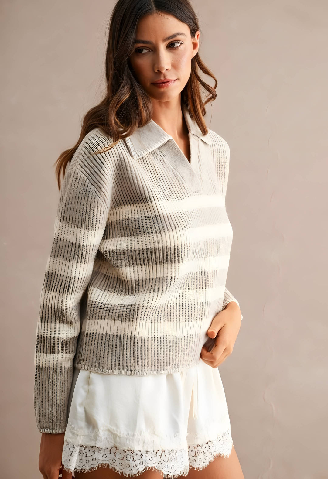 A woman wearing a beige and off-white horizontally striped ribbed knit polo sweater, styled with a white lace-trimmed skirt, against a neutral beige studio background.