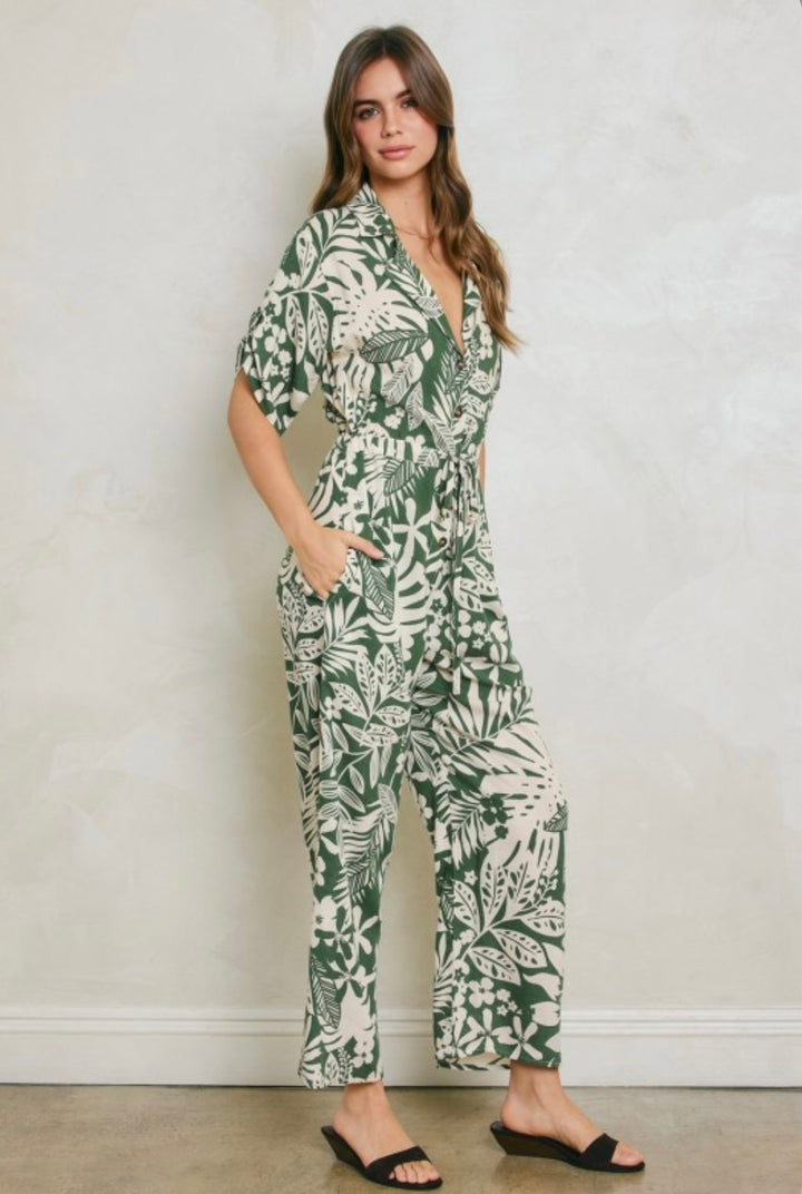 Woman wearing a green and white leaf-patterned jumpsuit against a plain background