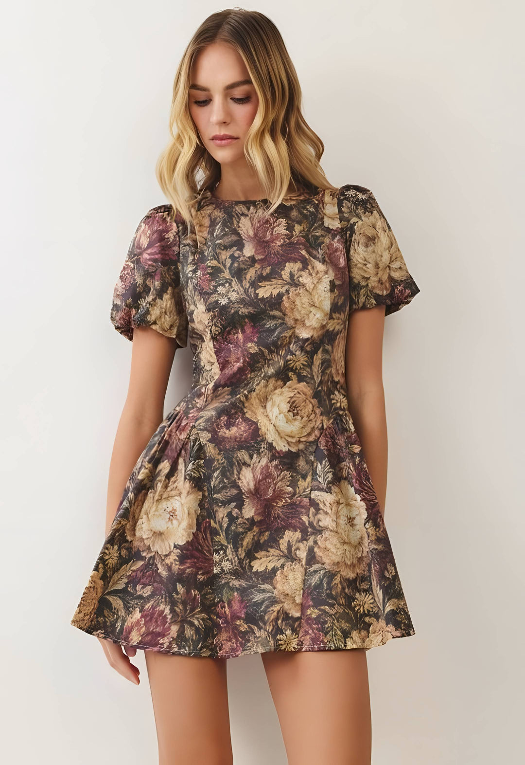 A woman wearing a short-sleeve floral mini dress with a puffed neckline and flared skirt, shown against a plain light background.