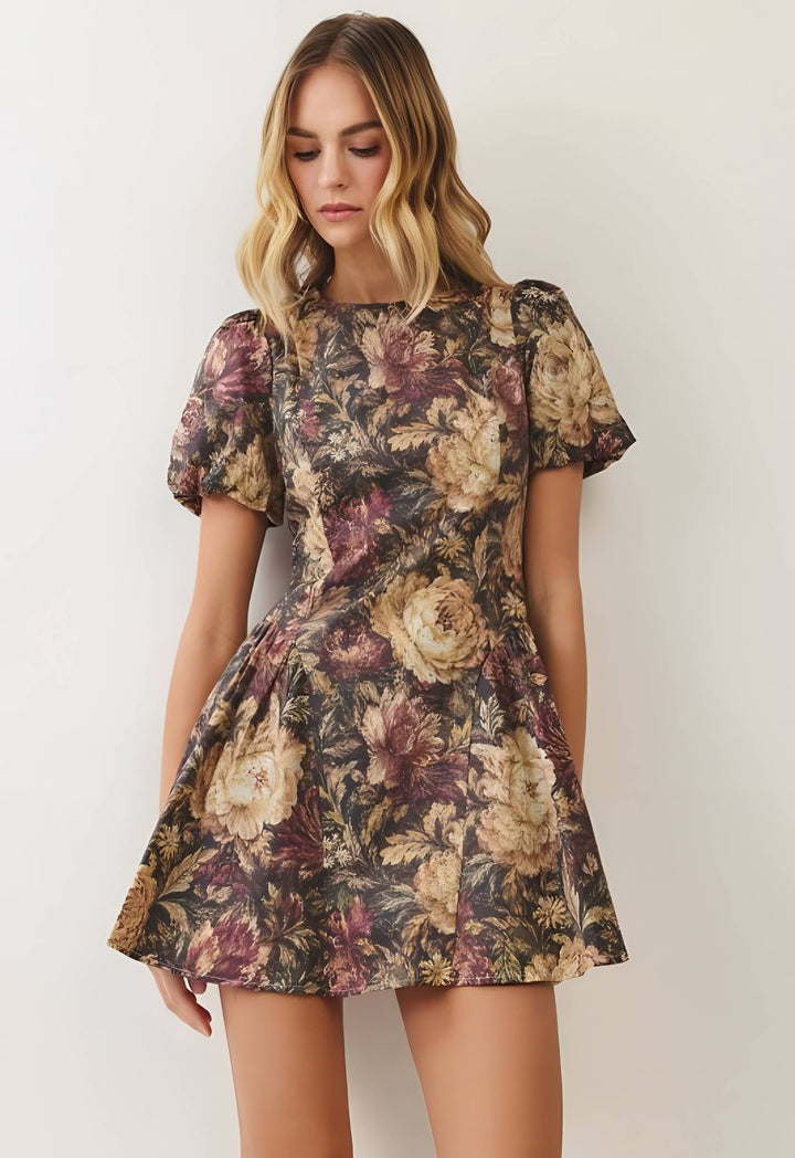 A woman wearing a short-sleeve floral mini dress with a puffed neckline and flared skirt, shown against a plain light background.