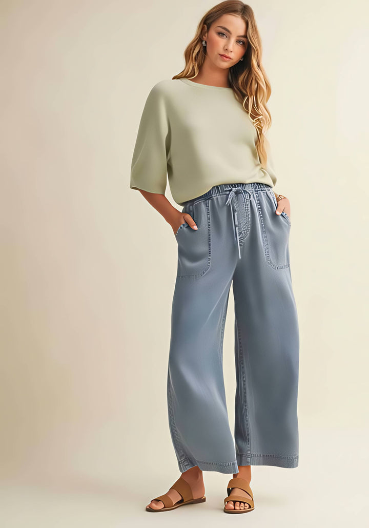 Woman wearing a light green top and blue wide-leg pants on a beige background