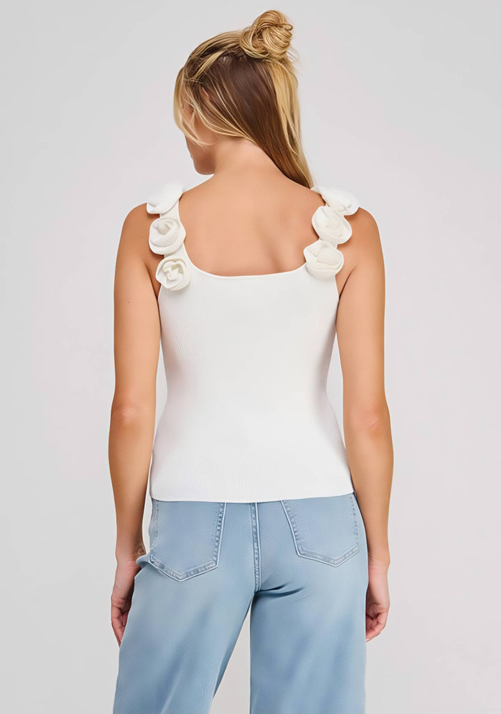 Woman wearing a white sleeveless top with floral details and light blue jeans on a plain background