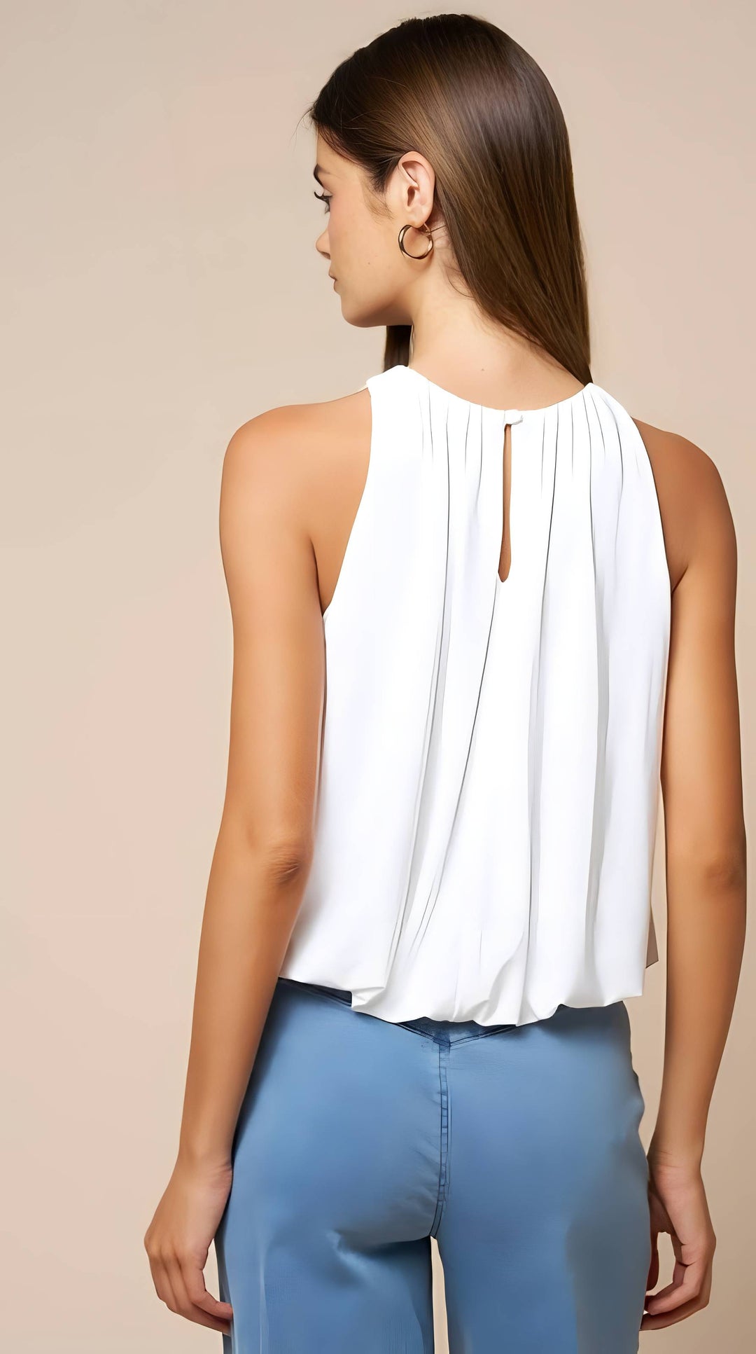 A woman shown from the back wearing a white sleeveless top with a gathered back keyhole detail and light blue pants, against a plain beige studio background.