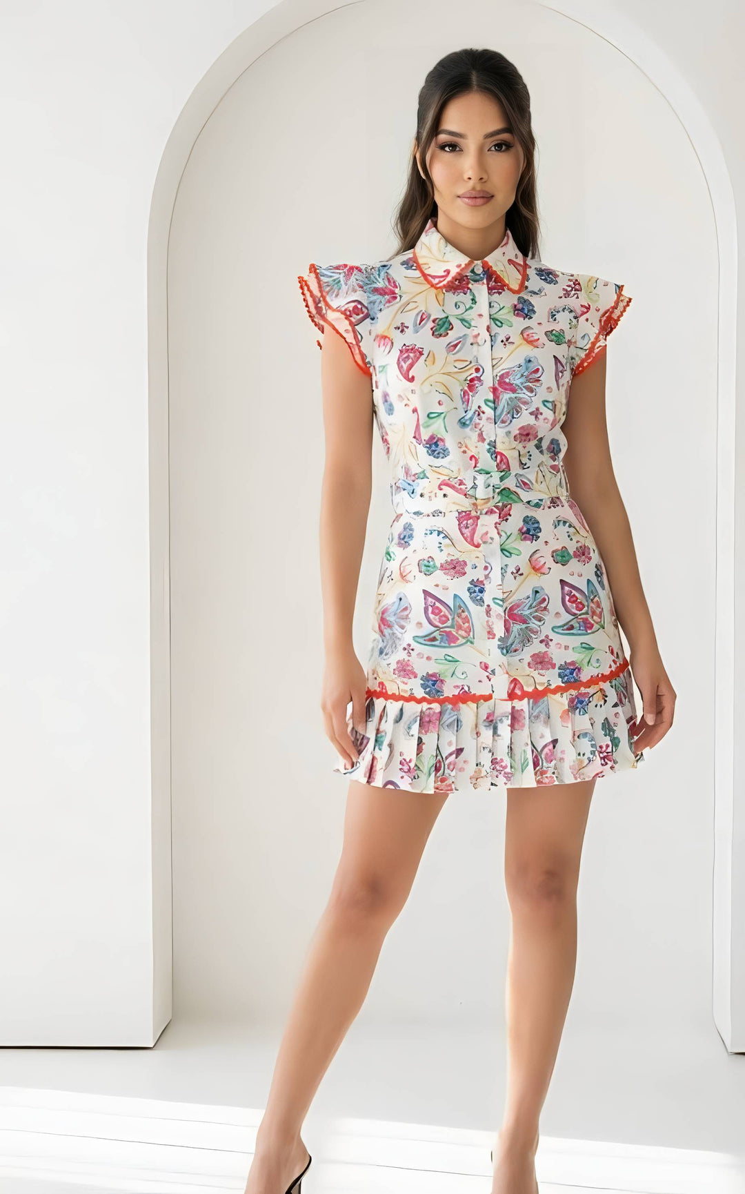 Woman wearing a colorful floral dress with ruffled sleeves and hem in a minimalistic setting.