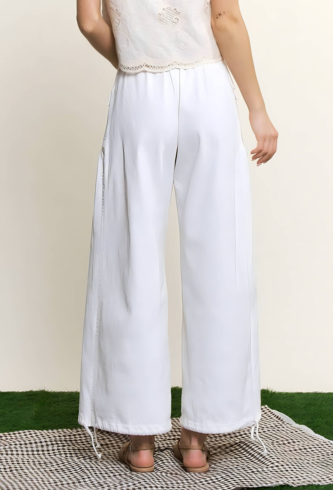 White wide-leg cropped pants with drawstring details at the ankles, shown on a model from the back against a cream background.
