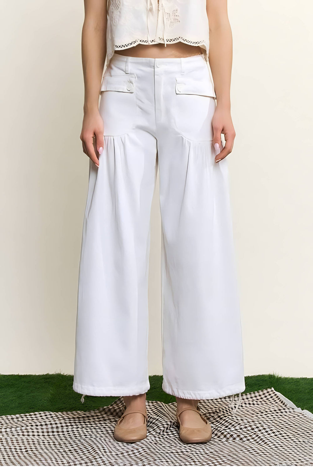 White wide-leg cropped pants with front flap pockets, shown on a model from the waist down wearing beige shoes against a cream background.