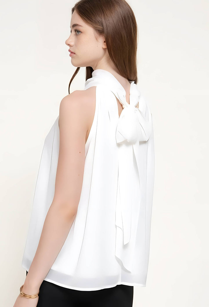 A woman shown from the back wearing a white sleeveless blouse with a large bow detail at the back neckline, paired with black bottoms, against a plain light background.