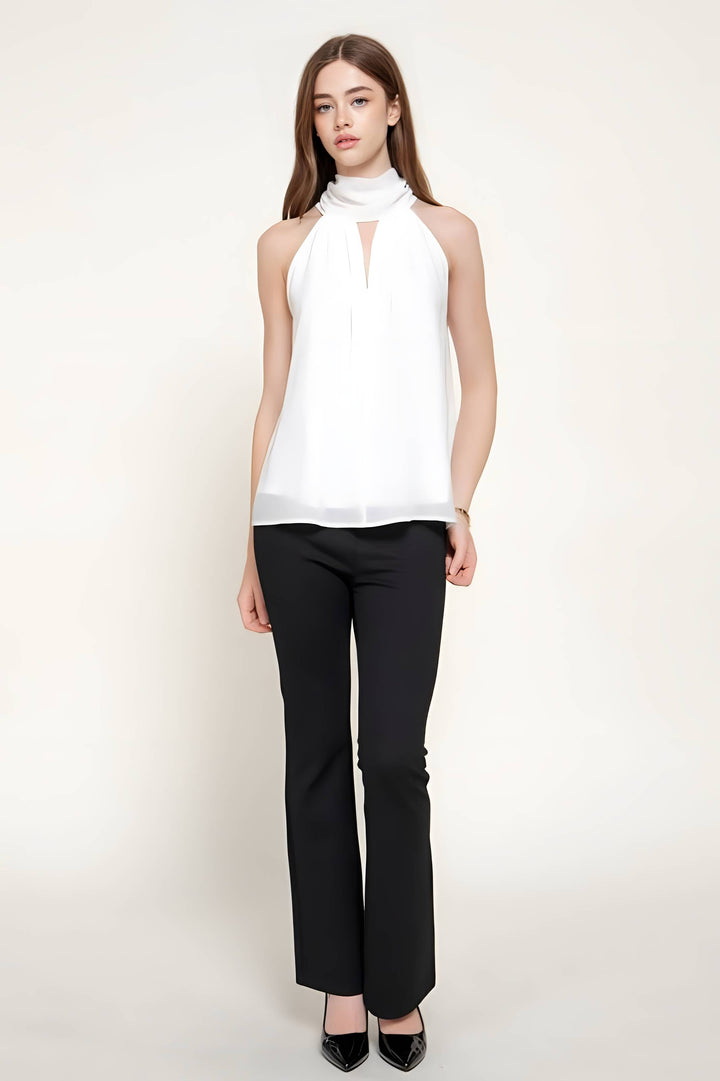 A woman modeling a white sleeveless halter-neck blouse with a keyhole cutout and black pants against a plain light background.