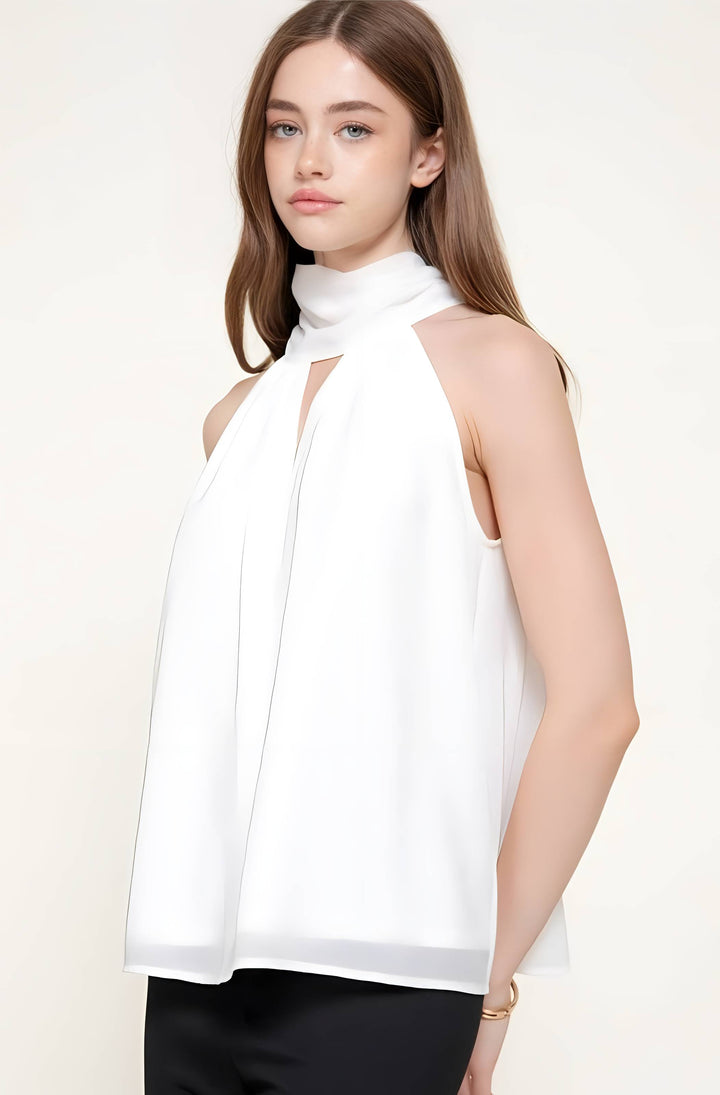 A woman modeling a white sleeveless mock neck top with a keyhole cutout at the chest, paired with black pants, against a plain off-white studio background.