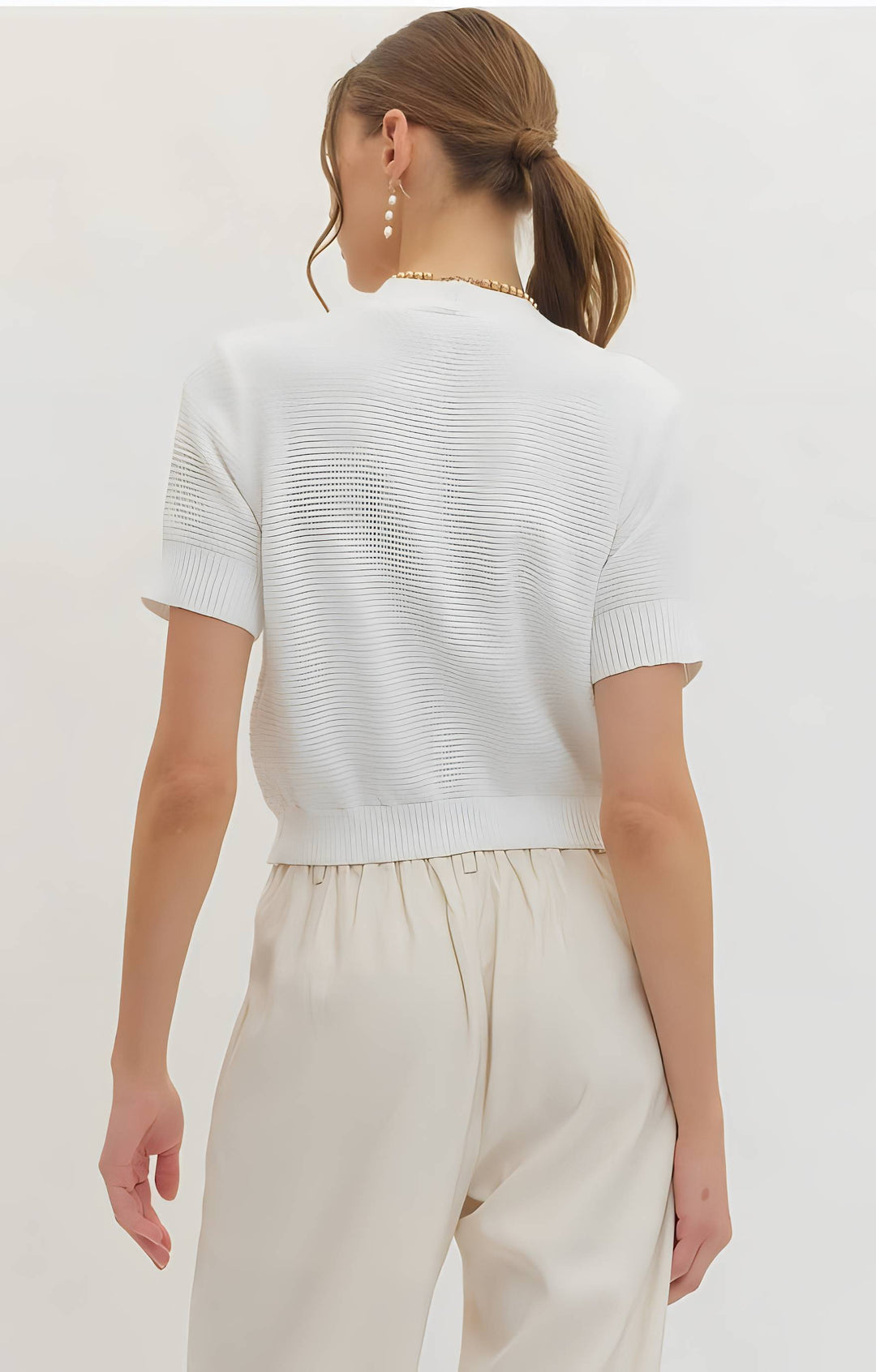 Woman wearing a white knit top and beige pants on a plain background