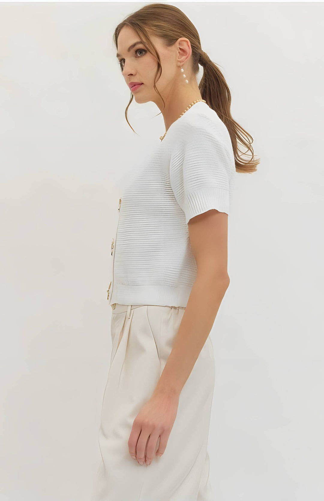 Woman wearing a white knit top and light-colored pants on a plain background
