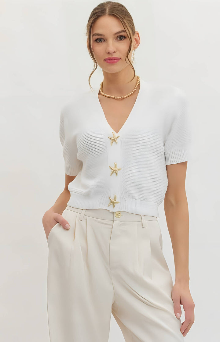 Woman wearing a white top with star designs and beige pants on a light gray background