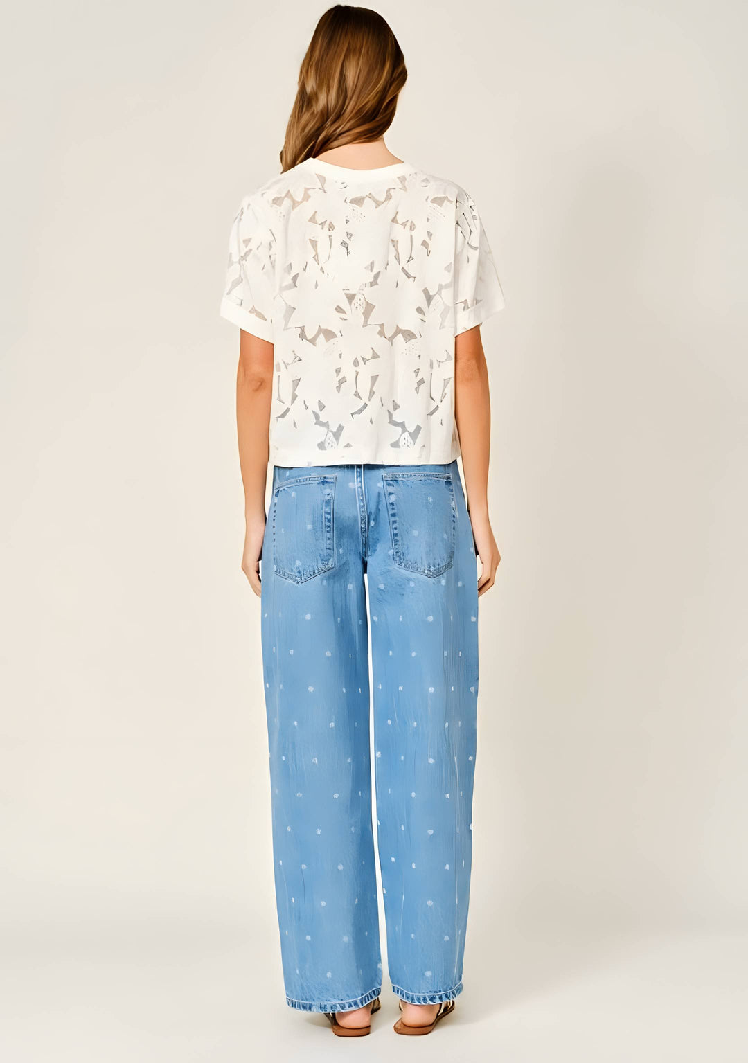 Woman wearing a white floral lace tee with jeans on a white background