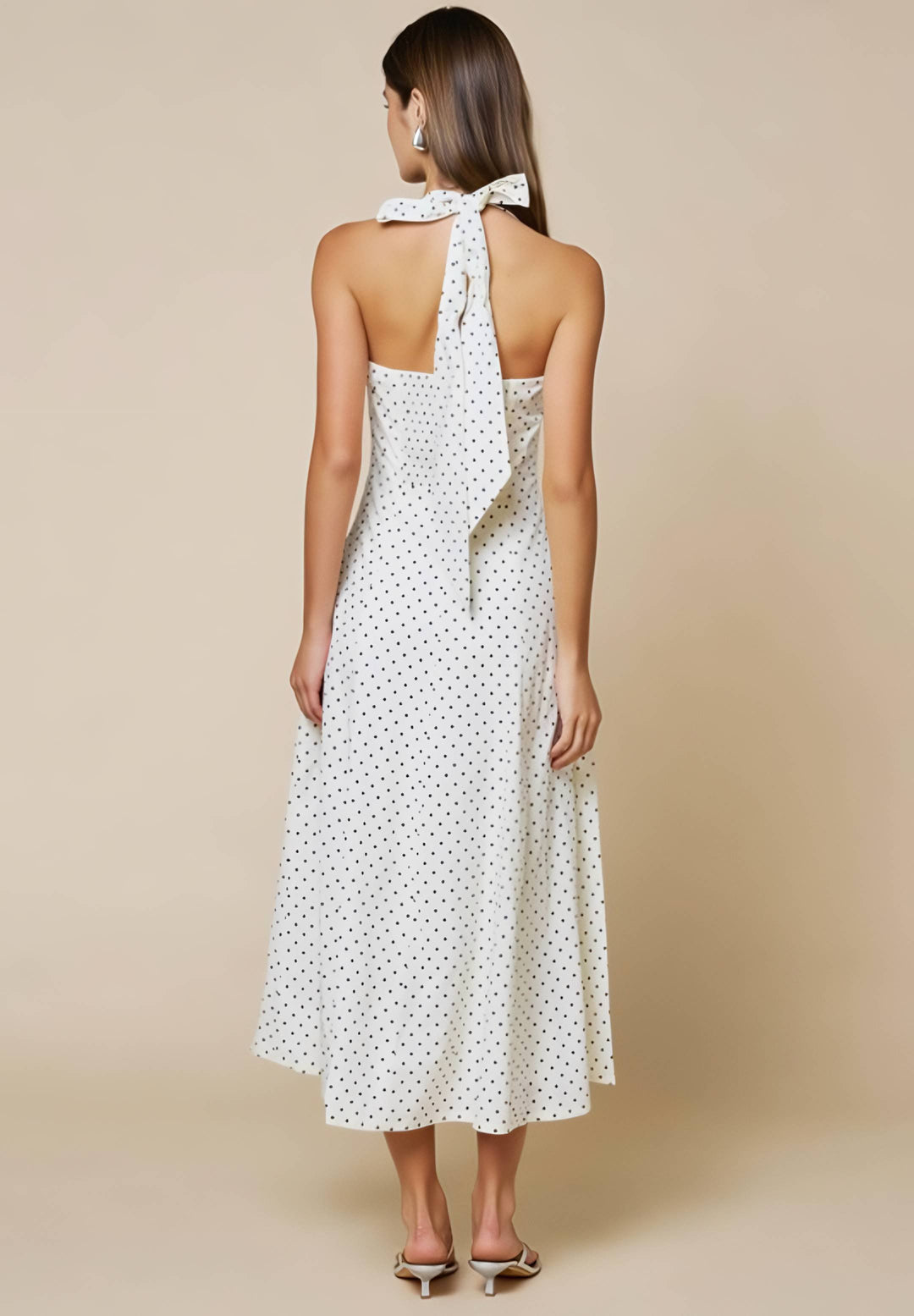 Woman wearing a white polka dot dress with a halter neck design on a beige background