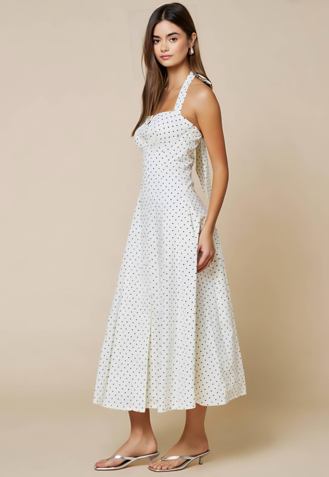 Woman wearing a white polka dot dress against a beige background