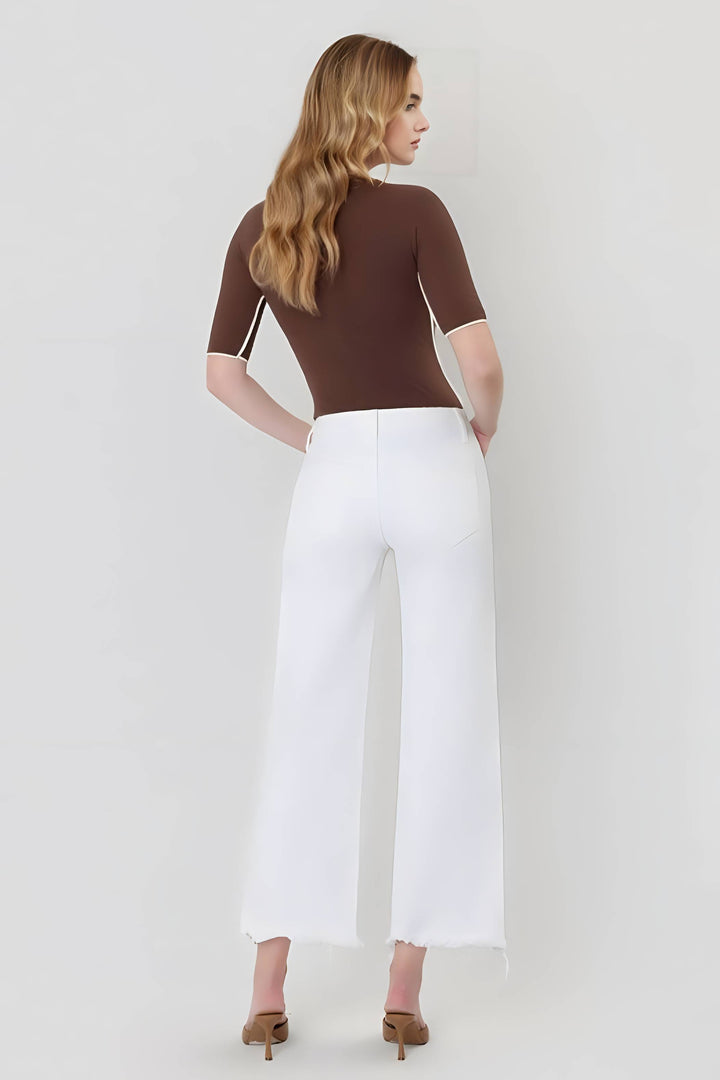Woman wearing a brown top and white pants on a plain background