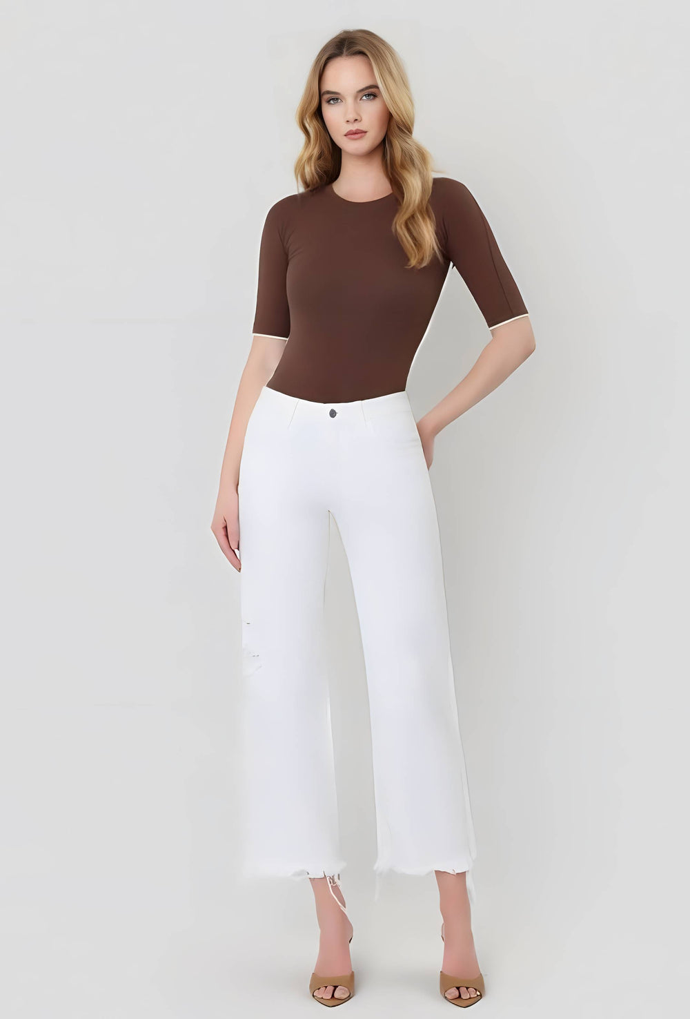 Woman wearing a brown top and white pants on a white background
