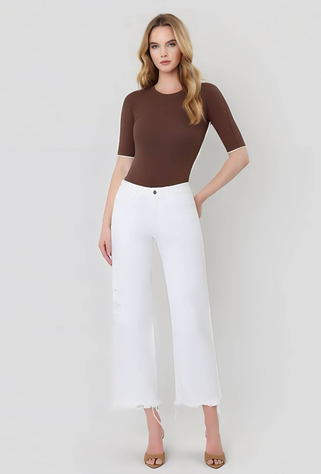 Woman wearing a brown top and white pants on a white background