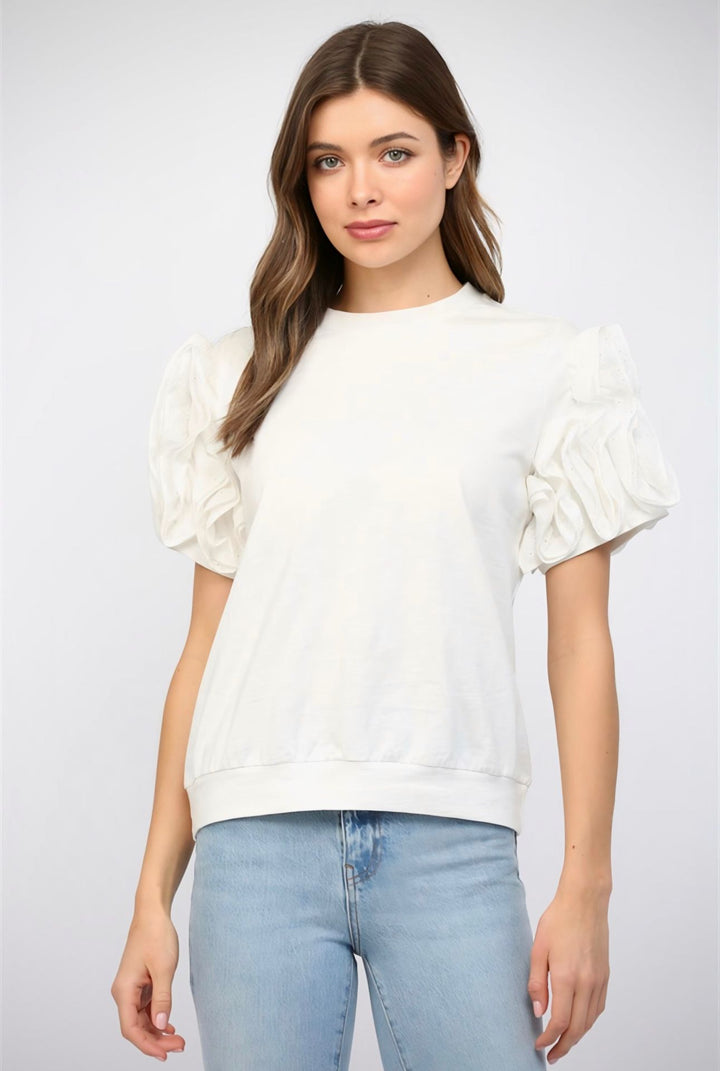 Woman wearing a white blouse with ruffled sleeves and light blue jeans on a plain background