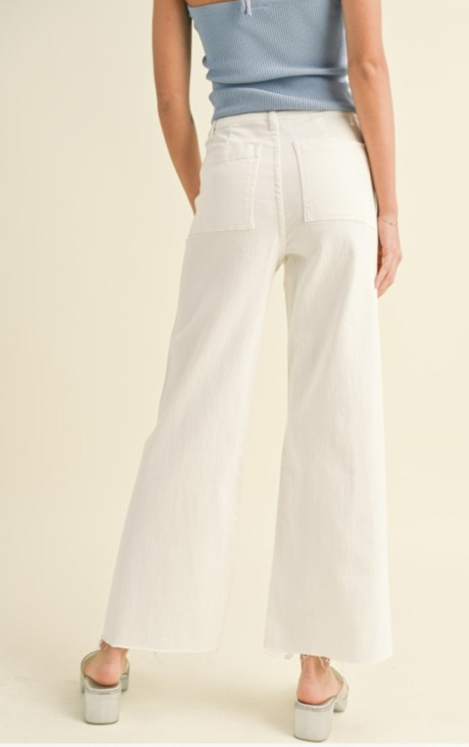 Person wearing white wide-leg pants and a light blue top on a beige background