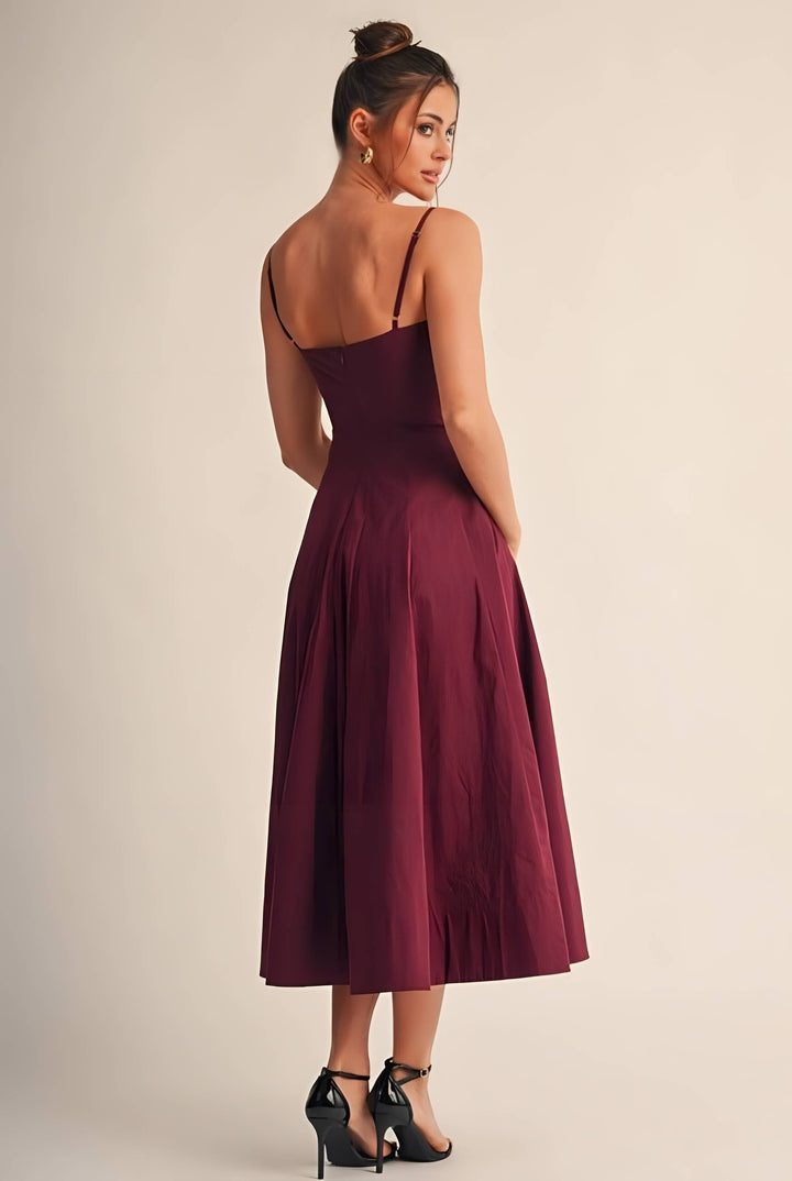 A woman wearing a sleeveless midi dress in deep burgundy, shown from the back. The dress features thin spaghetti straps, a structured waist, and a flared skirt.