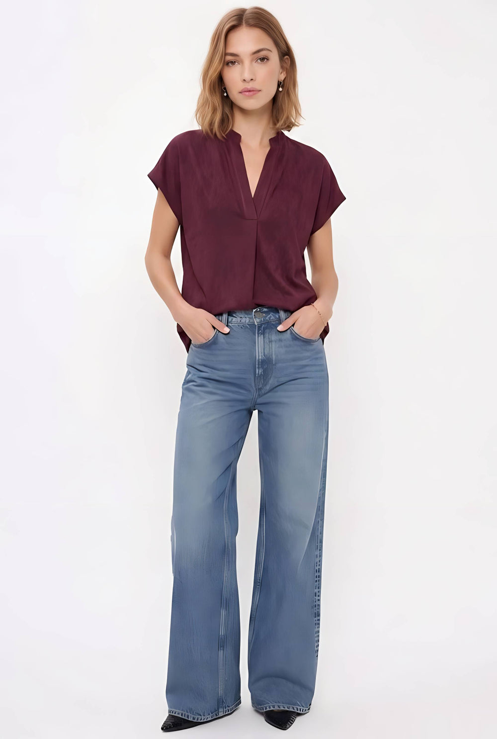 A woman modeling a short-sleeve burgundy blouse and wide-leg blue jeans against a plain white studio background.