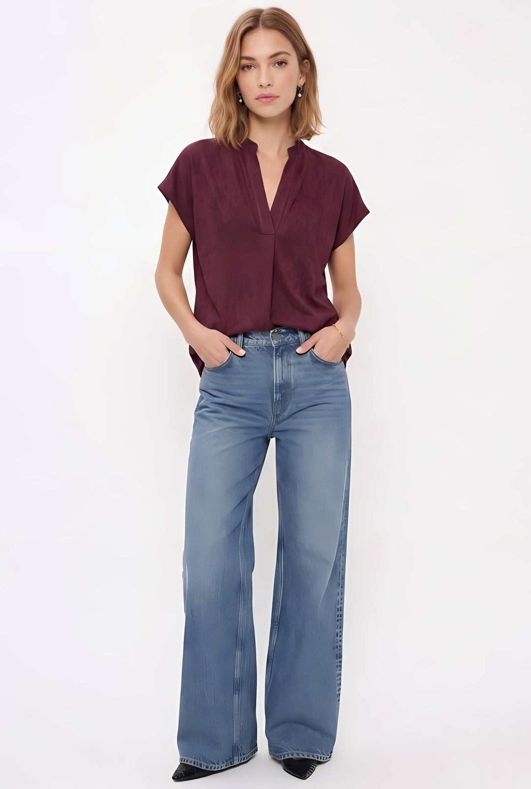 A woman modeling a short-sleeve burgundy blouse and wide-leg blue jeans against a plain white studio background.