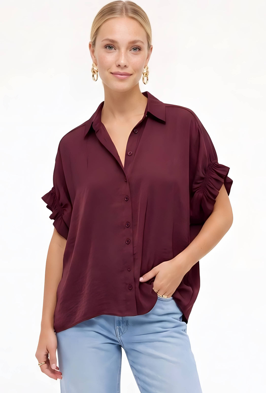 A woman modeling a dark burgundy button-up blouse with ruffled sleeves, paired with light blue jeans, against a plain white background.