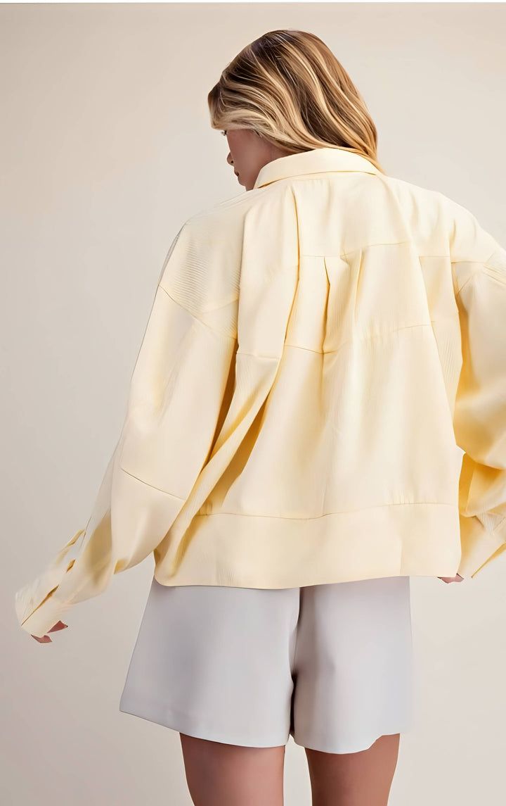 Person wearing a light yellow jacket and white shorts on a plain background