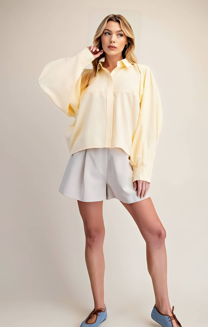 Woman wearing a light yellow oversized shirt and white shorts on a plain background