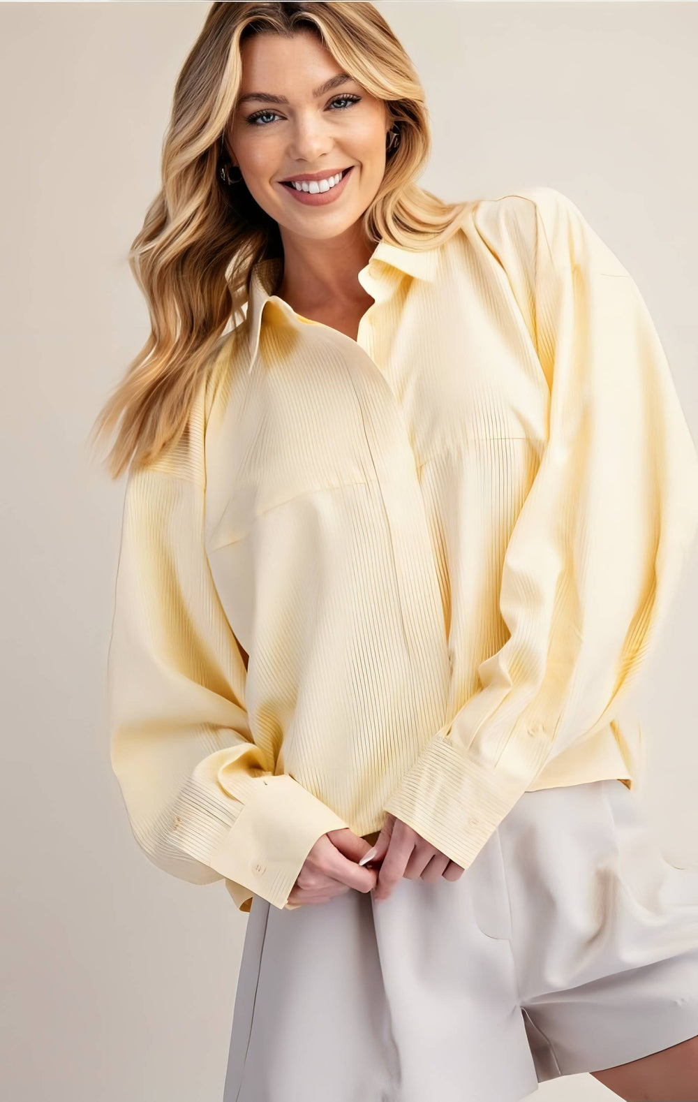 Woman wearing a light yellow blouse and white pants against a beige background