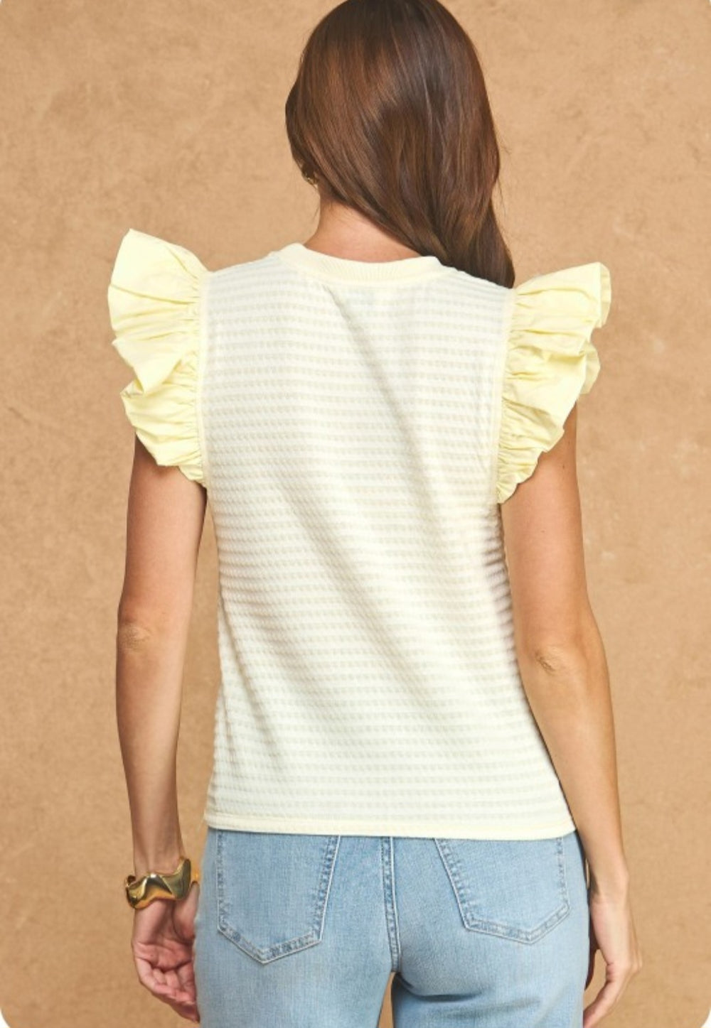 Woman wearing a light yellow top with ruffled sleeves against a beige background