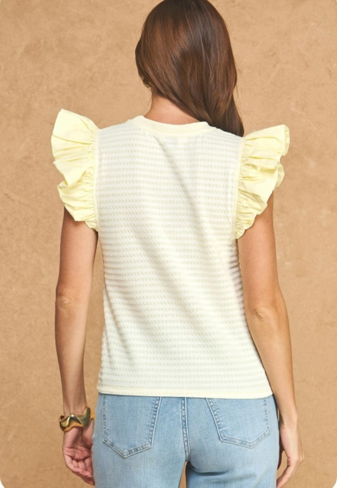 Woman wearing a light yellow top with ruffled sleeves against a beige background