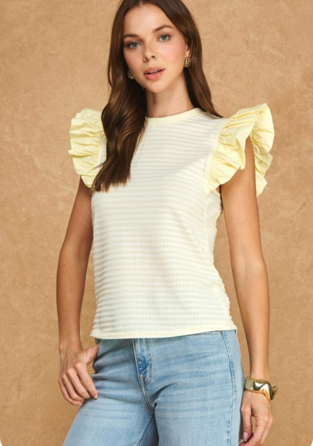 Woman wearing a white top with yellow ruffled sleeves against a beige background